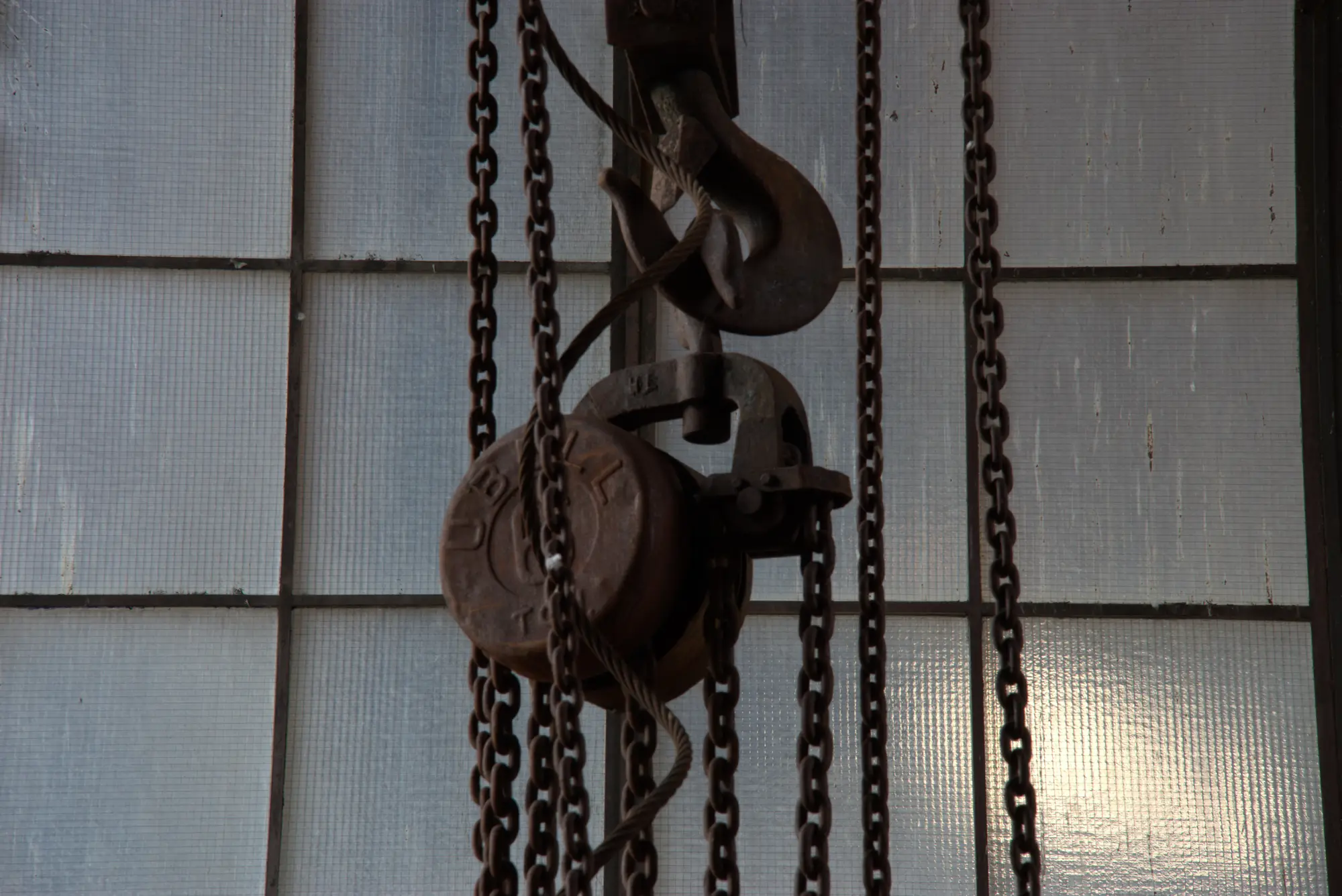 Der Flaschenzug hängt an seiner Kette, vor der Glasbausteinwand.
